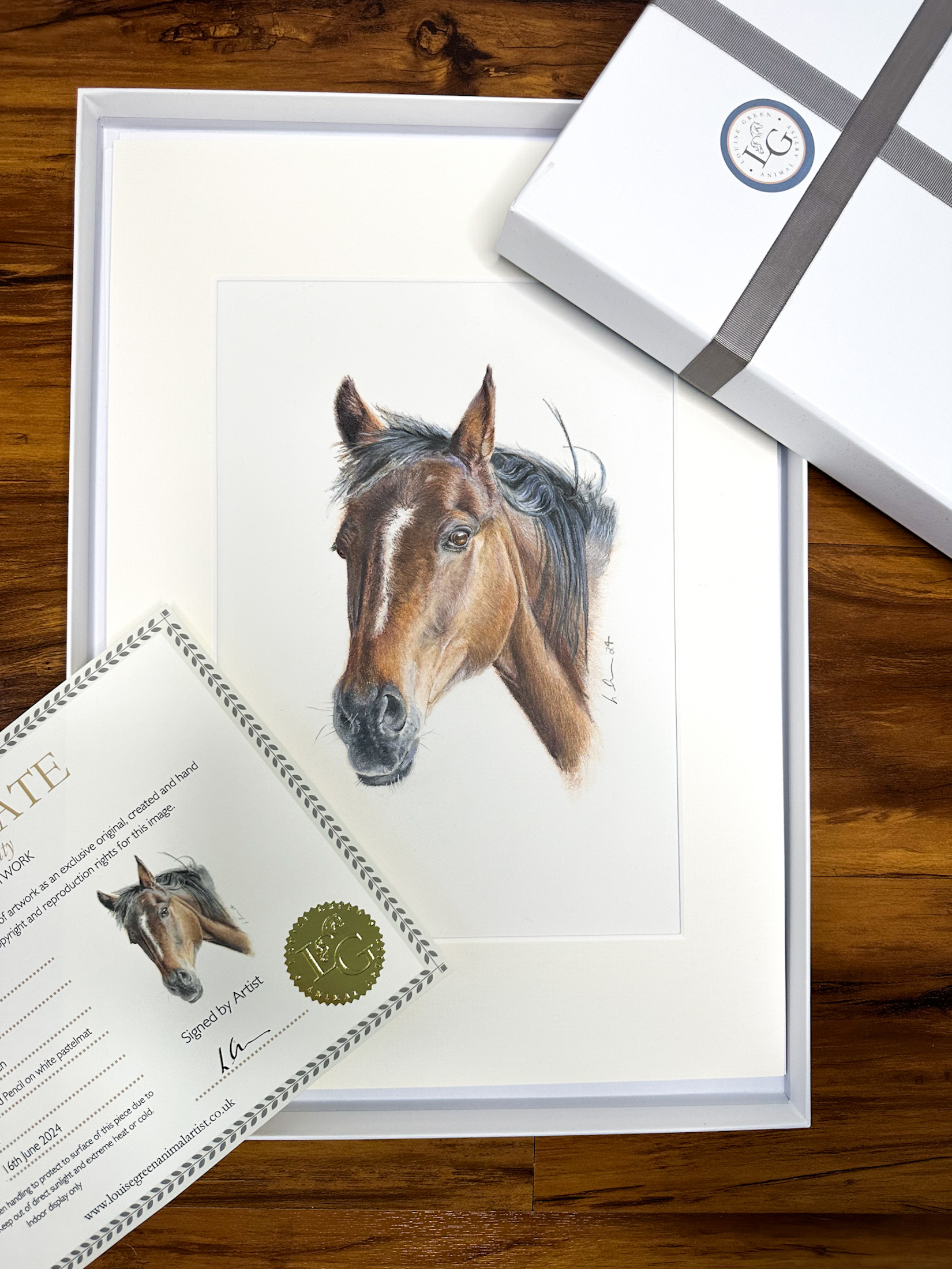 Colour pencil horse portrait of a brown horse in an off white mount and boxed in a white gift box. The lid of the box and part of certificate of authentication is also shown