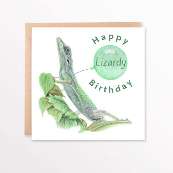Colour pencil green lizard drawing sitting on some leaves. There is a plain white background and the lizard is holding a green balloon. The text says Happy Lizardy Birthday, with the word Lizardy inside the balloon. The artwork is on a square card laid flat on top of a brown envelope