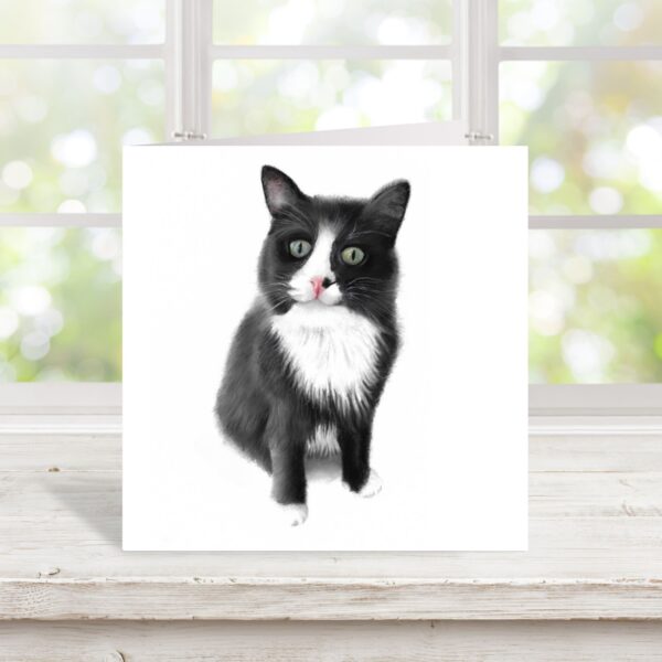 Colour pencil drawing of a black and white fluffy cat. The cat has a white bib and white nose with white paws. The cat is sitting down and whole cat has been drawn with the two front legs included. The artwork is on a square card displayed on a pale wooden window sill in front of a window frame.