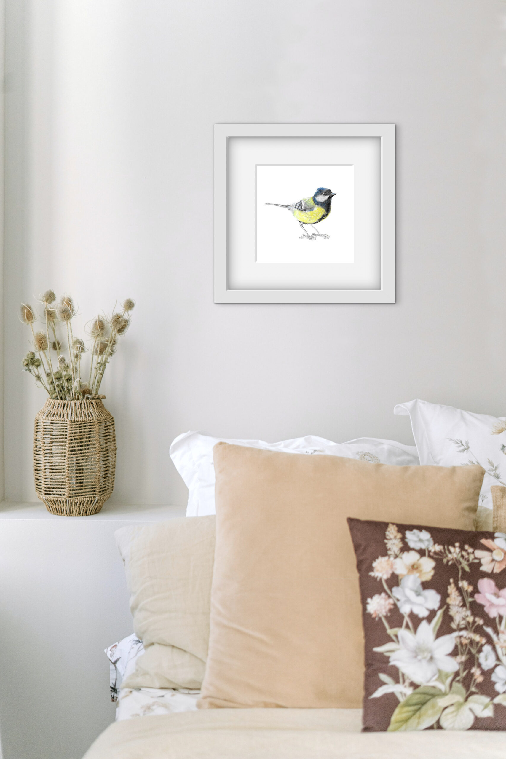 colour pencil art of a small great tit bird in a square white frame on a wall above a sofa with cushions