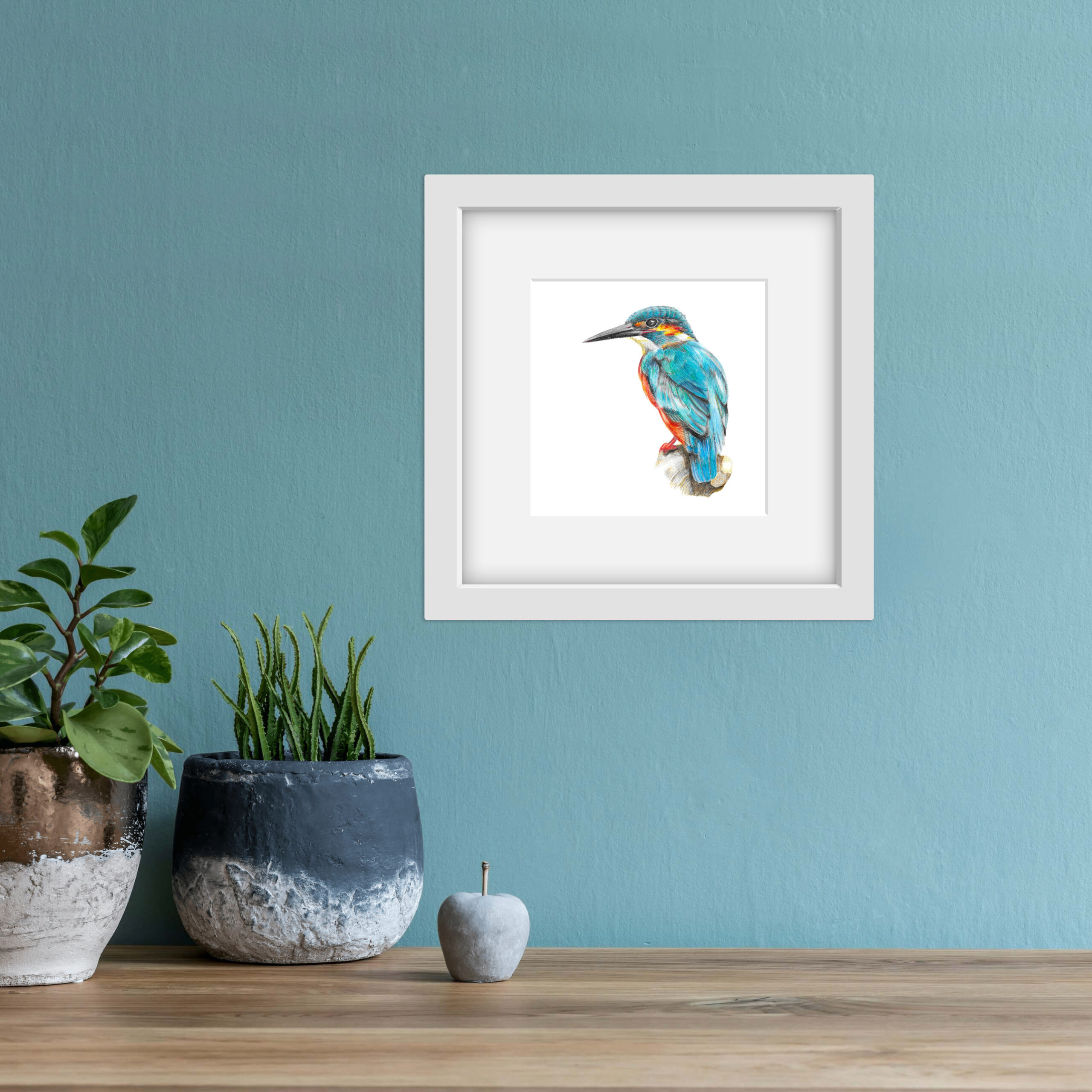 colour pencil drawing of a kingfisher in a square white frame in a blue room with plants